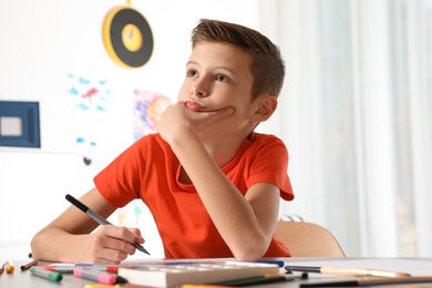 Photo of Little child drawing picture at table with painting tools indoors