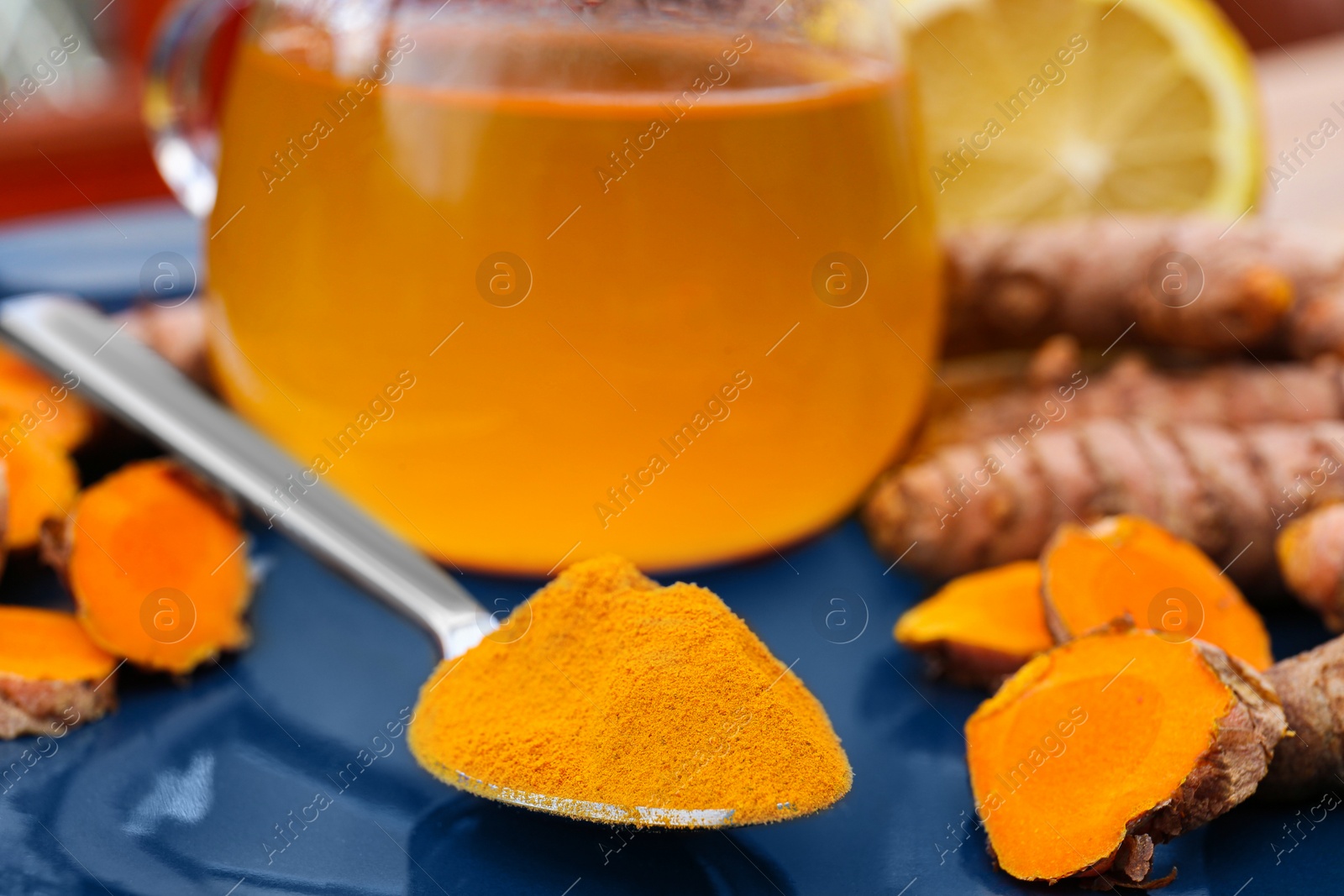 Photo of Plate with glass cup of hot tea, lemon, turmeric powder and roots on table, closeup