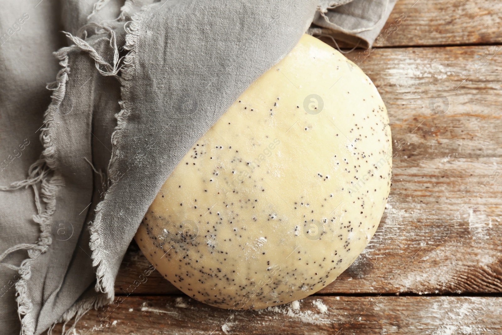 Photo of Raw dough with poppy seeds under towel on wooden table