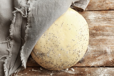 Raw dough with poppy seeds under towel on wooden table