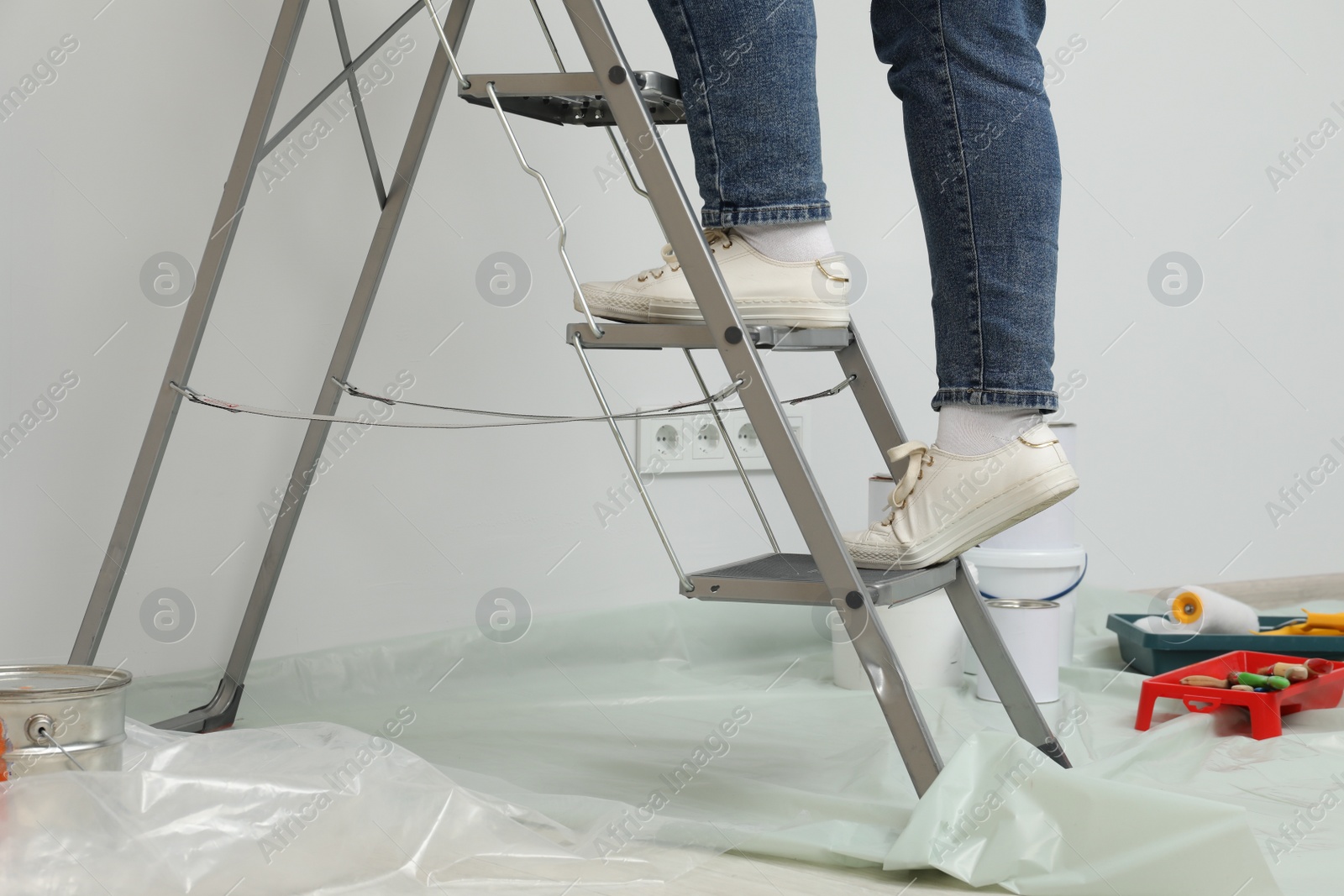Photo of Woman standing on metallic folding ladder and painting tools, closeup