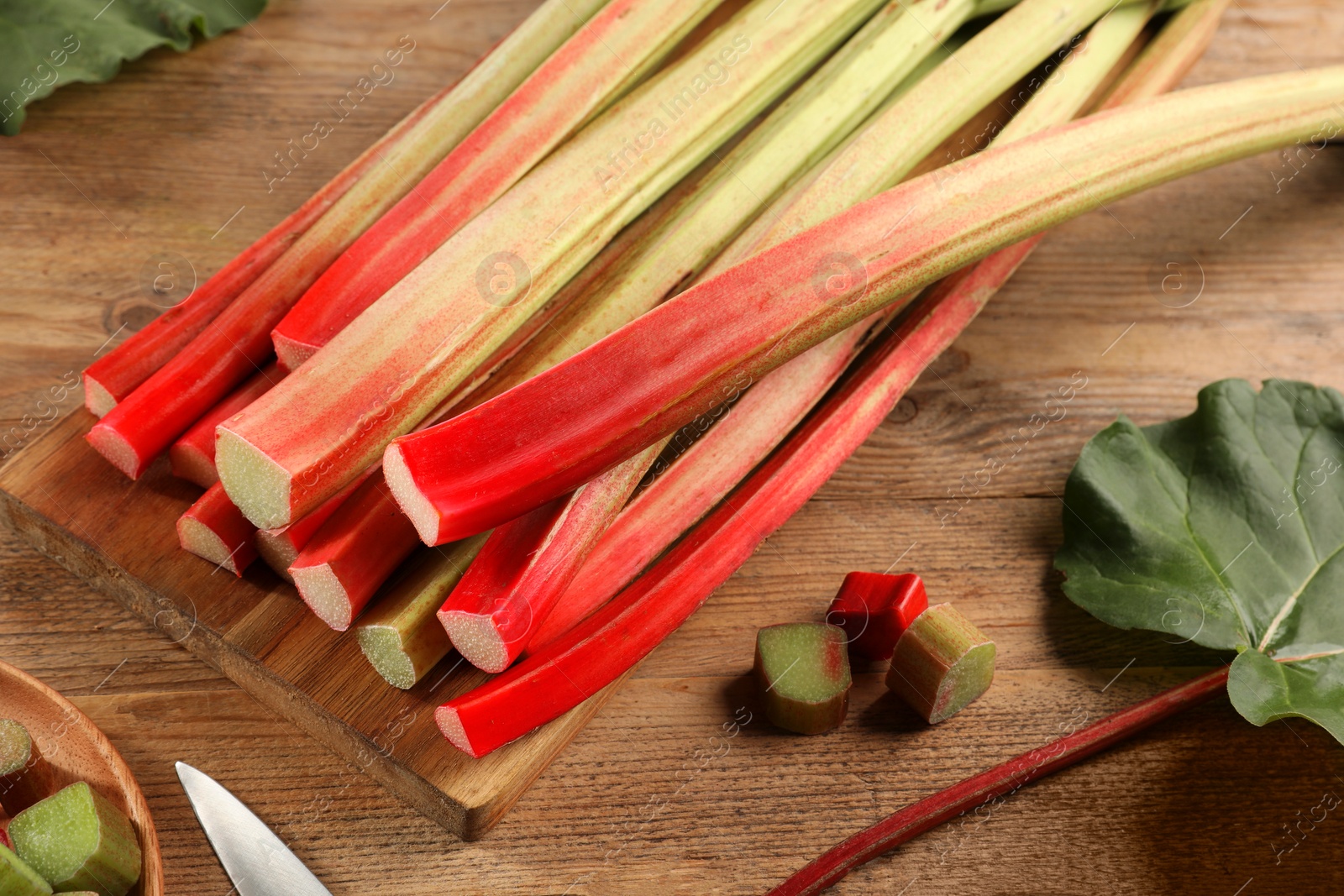 Photo of Many cut rhubarb stalks and leaf on wooden table, closeup