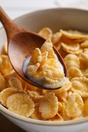 Photo of Spoon with tasty cornflakes and milk over bowl, closeup