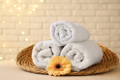 Photo of Rolled terry towels and flower on white table near brick wall indoors, space for text