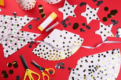 Photo of Handmade party hat templates, confetti and tools on red background, flat lay
