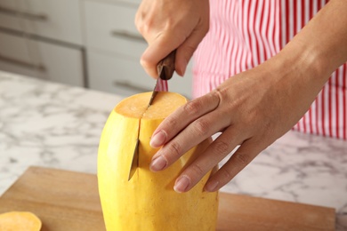 Photo of Woman cutting ripe spaghetti squash on table in kitchen, closeup