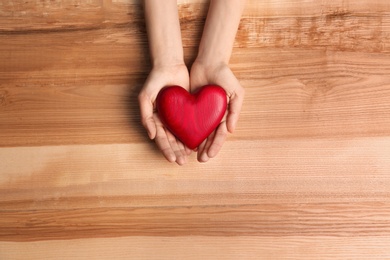 Woman holding decorative heart on wooden background, top view. Space for text