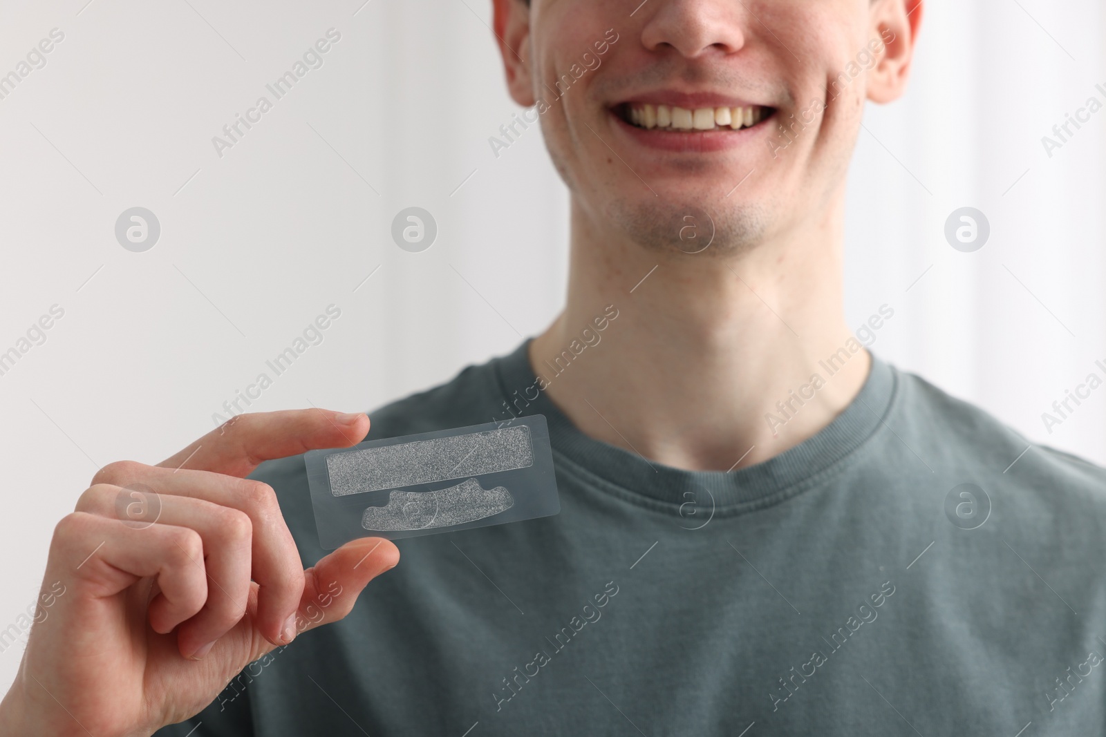 Photo of Young man with whitening strips on light background, closeup