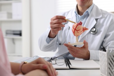 Gastroenterologist with human stomach model consulting patient at table in clinic, closeup