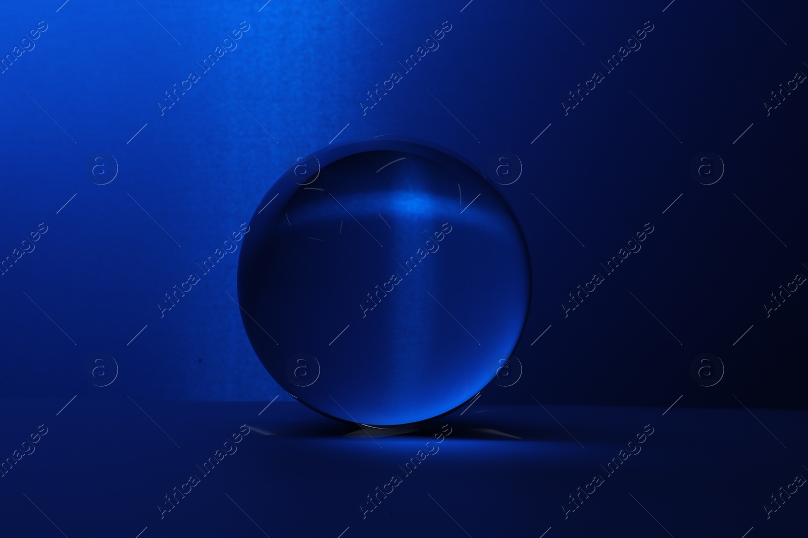 Photo of Transparent glass ball on table against blue background