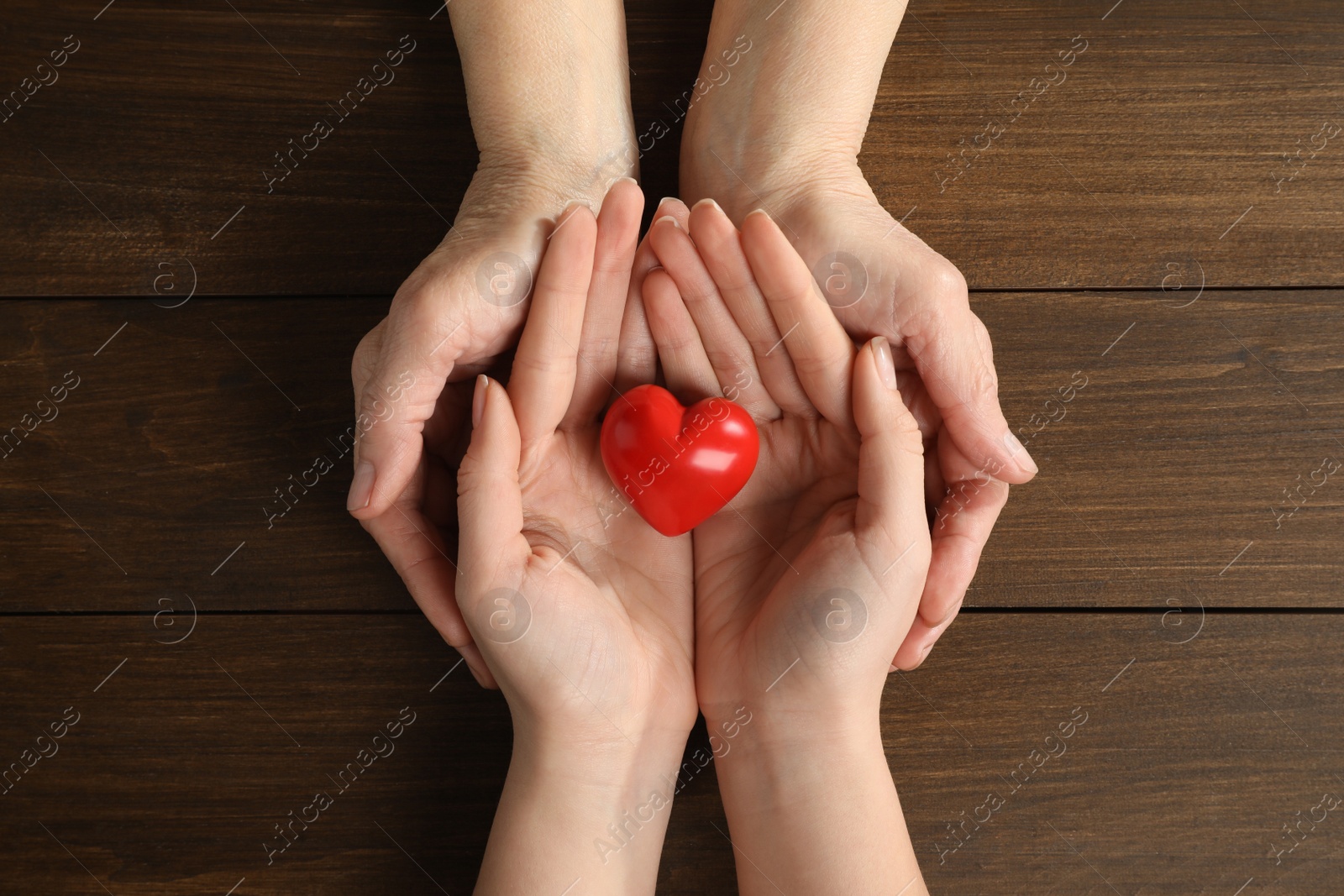Photo of Young and elderly women holding red heart at wooden table, top view