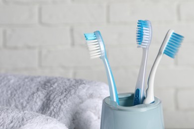 Photo of Plastic toothbrushes in holder and towels near white brick wall, closeup