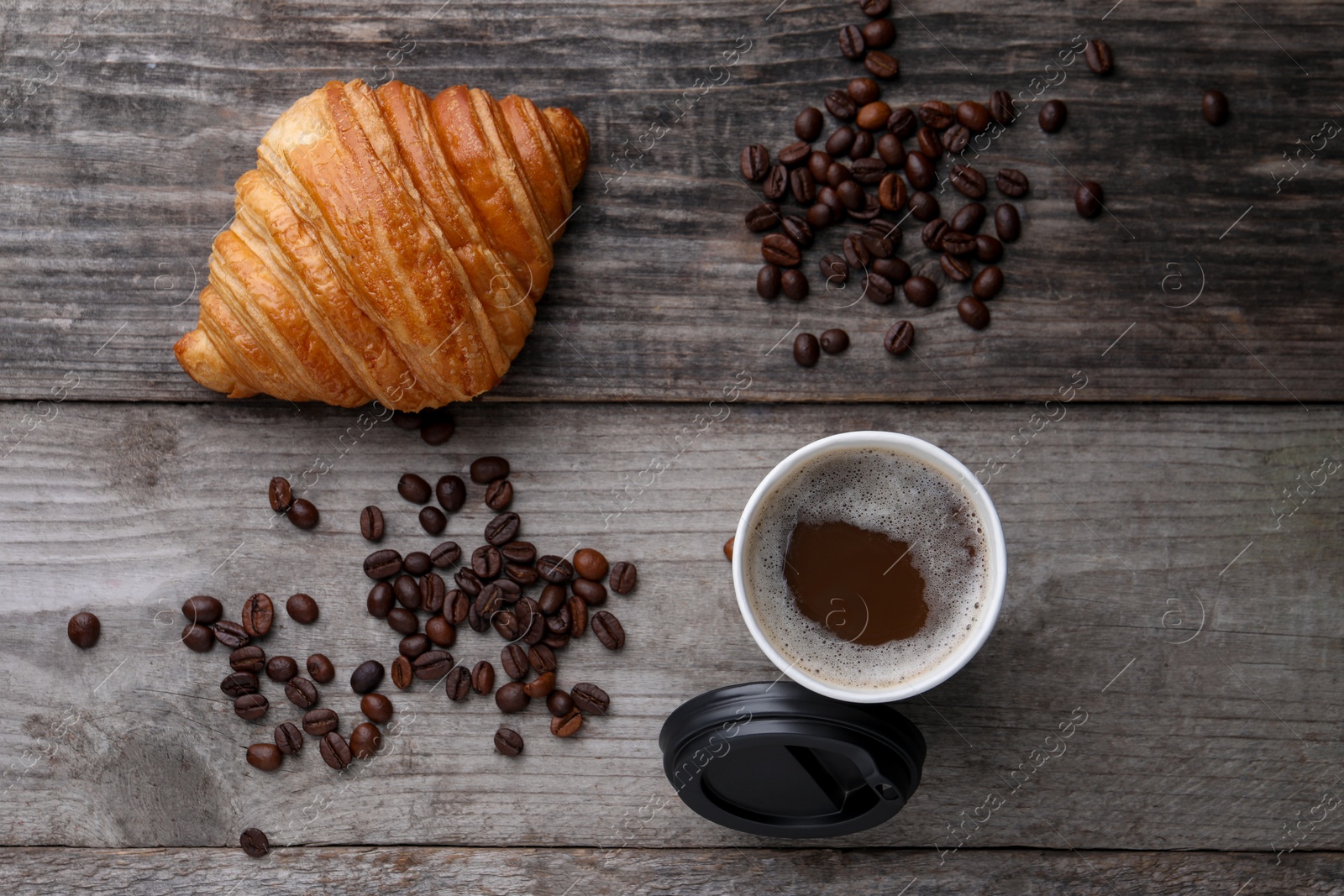 Photo of Coffee to go. Paper cup with tasty drink, croissant and beans on wooden table, flat lay