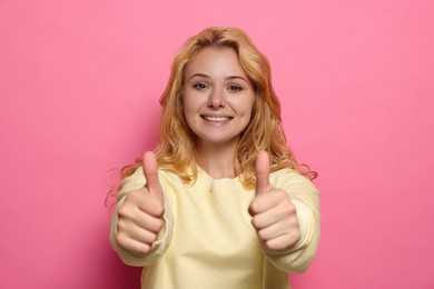 Photo of Happy young woman showing thumbs up on pink background