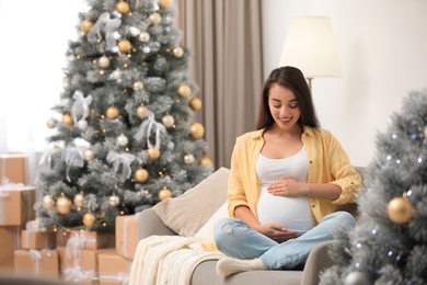 Happy pregnant woman on sofa in living room decorated for Christmas. Expecting baby