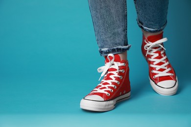 Photo of Woman wearing pair of new stylish sneakers on light blue background, closeup. Space for text