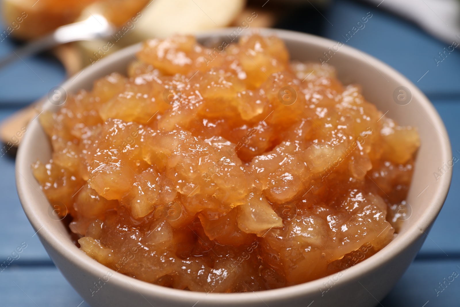 Photo of Bowl with delicious apple jam on blue wooden table, closeup