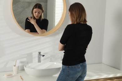 Sad young woman near mirror in bathroom