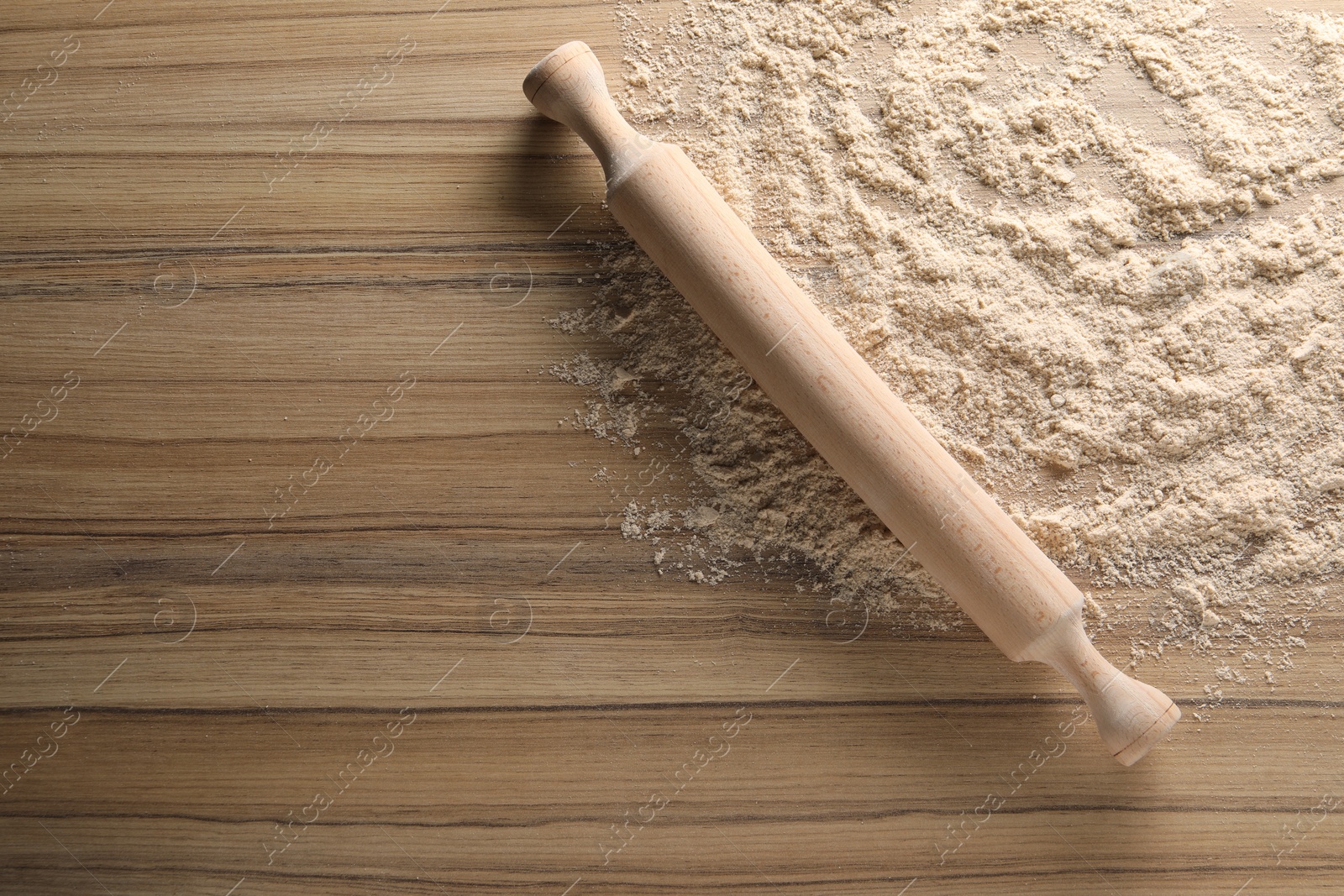 Photo of Scattered flour and rolling pin on wooden table, top view. Space for text