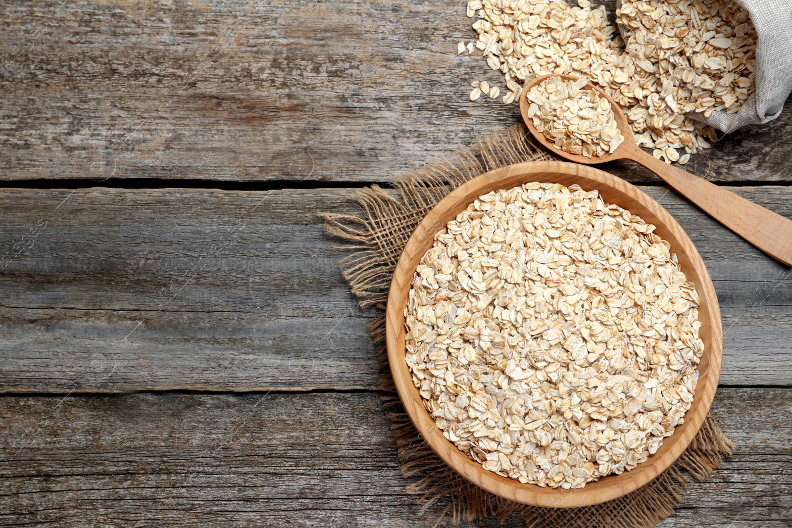 Photo of Oatmeal, bowl, spoon and bag on wooden table, flat lay. Space for text