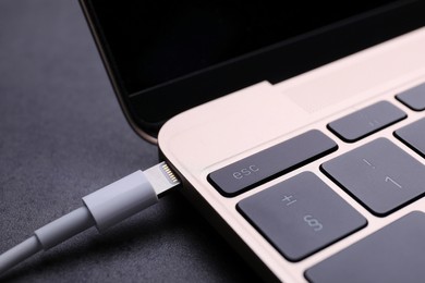 Photo of USB cable with lightning connector and laptop on black table, closeup