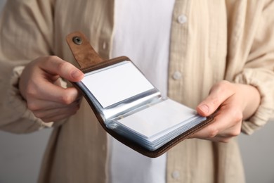 Woman holding leather business card holder with blank cards on grey background, closeup