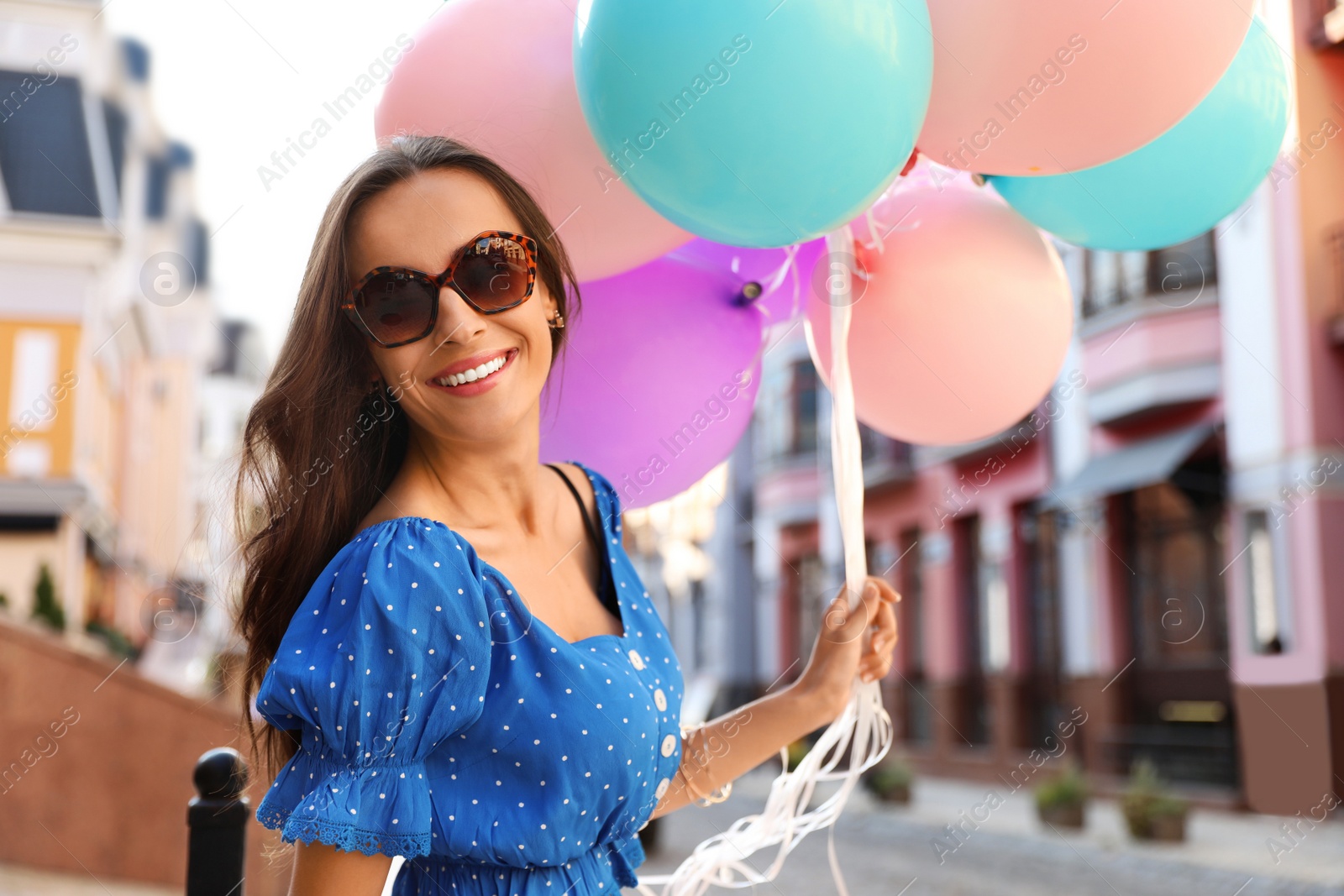 Photo of Beautiful young woman with color balloons on city street