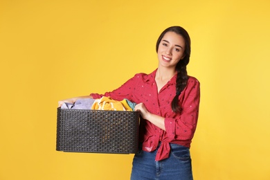 Happy young woman holding basket with clothes on color background