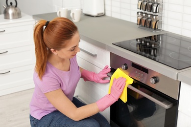 Woman cleaning modern oven with rag in kitchen