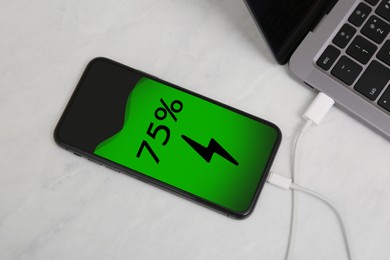 Image of Smartphone connected with charge cable to laptop on light table, above view