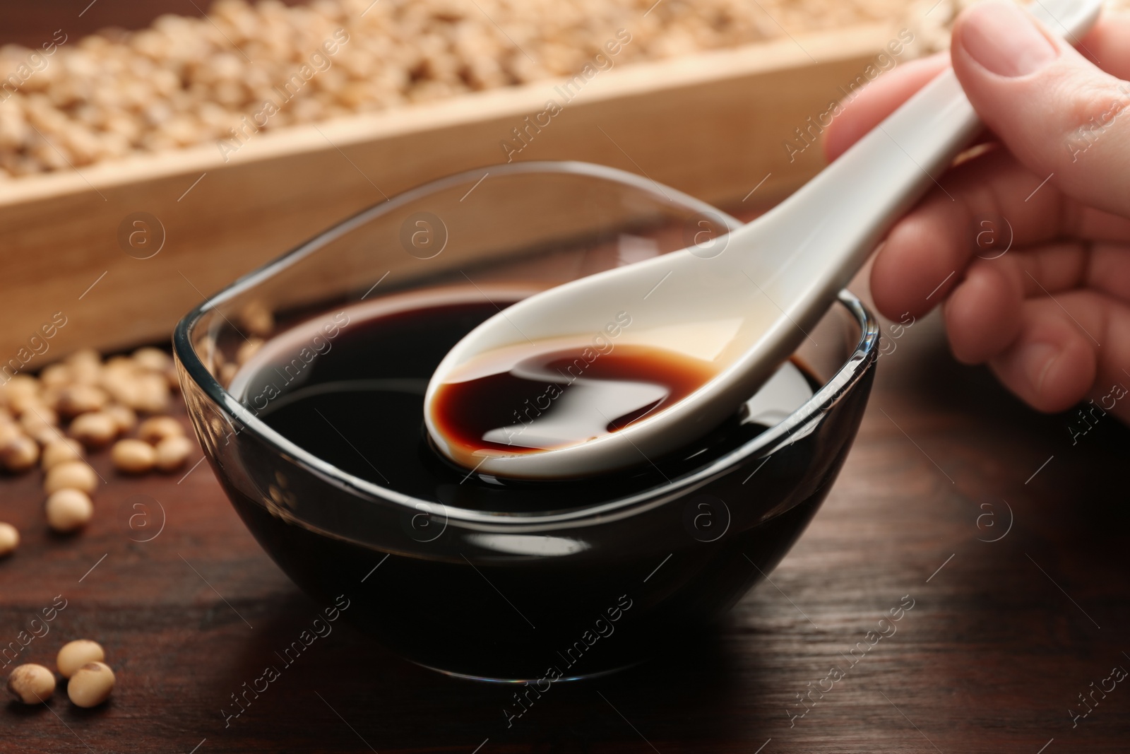 Photo of Woman taking soy sauce with spoon from bowl at wooden table, closeup