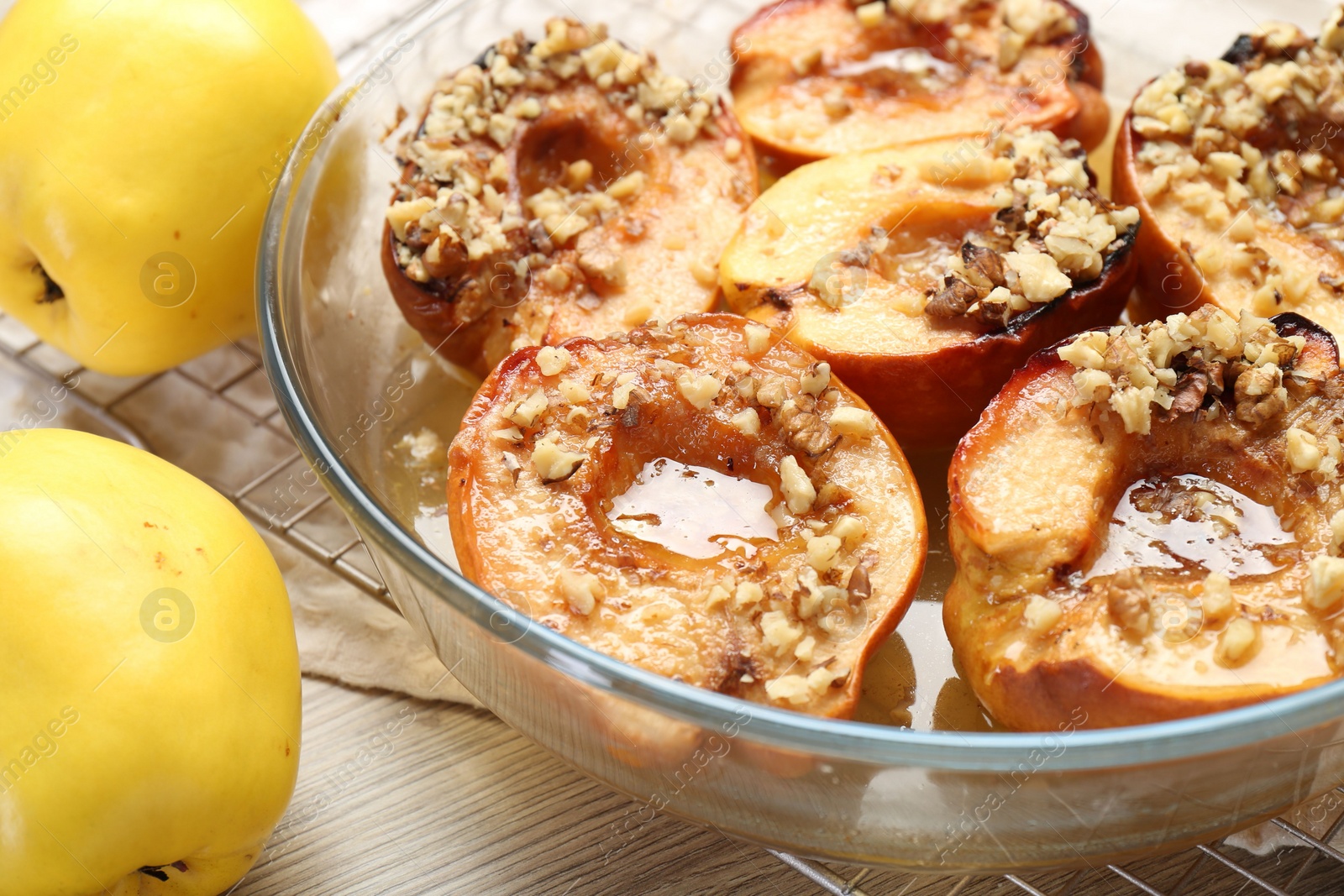 Photo of Delicious baked quinces with nuts in bowl and fresh fruits on wooden table, closeup