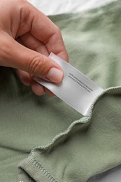 Photo of Woman holding clothing label on olive garment, closeup