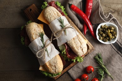 Photo of Delicious sandwiches with bresaola, lettuce and other products on wooden table, flat lay