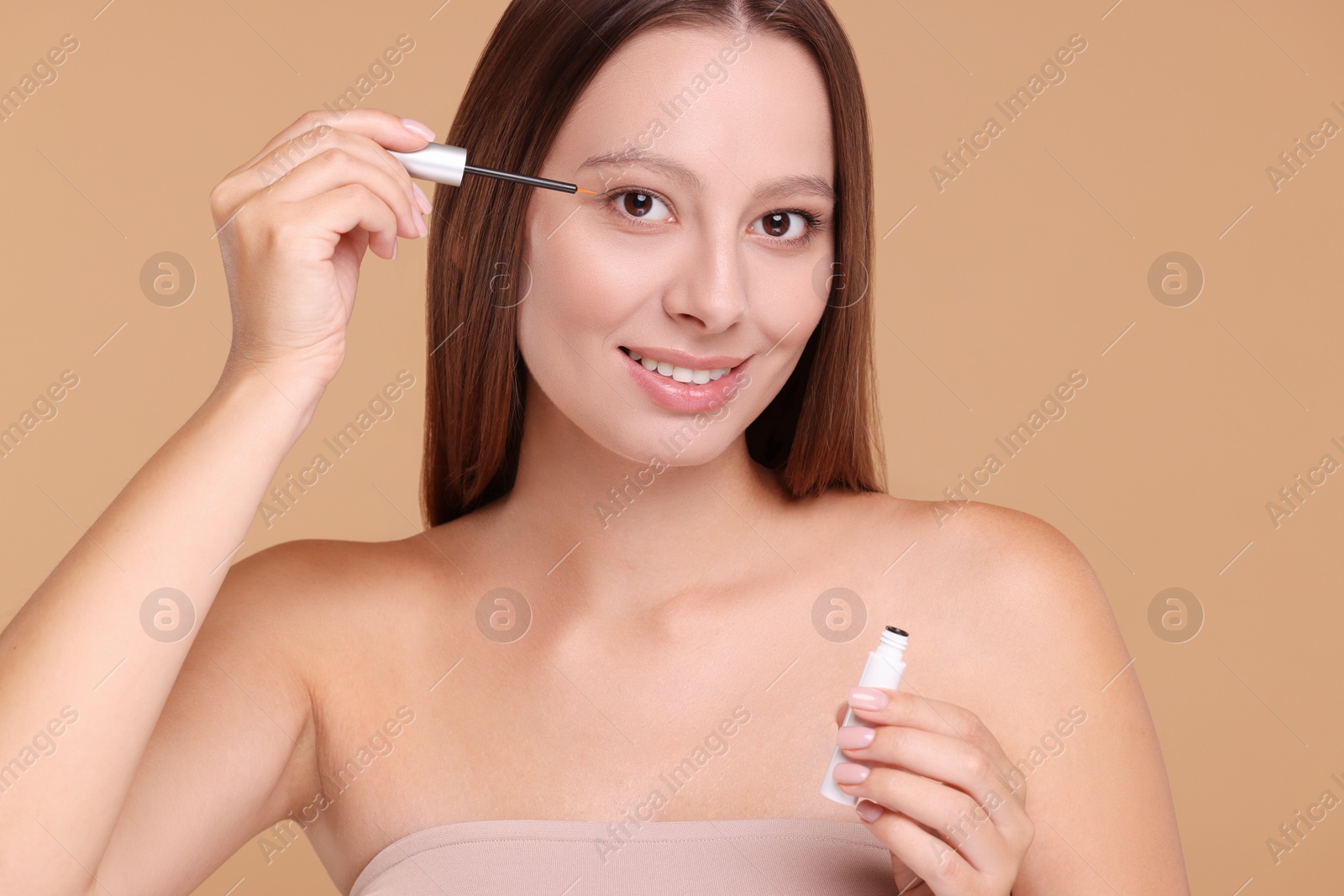 Photo of Beautiful woman applying serum onto eyelashes on beige background