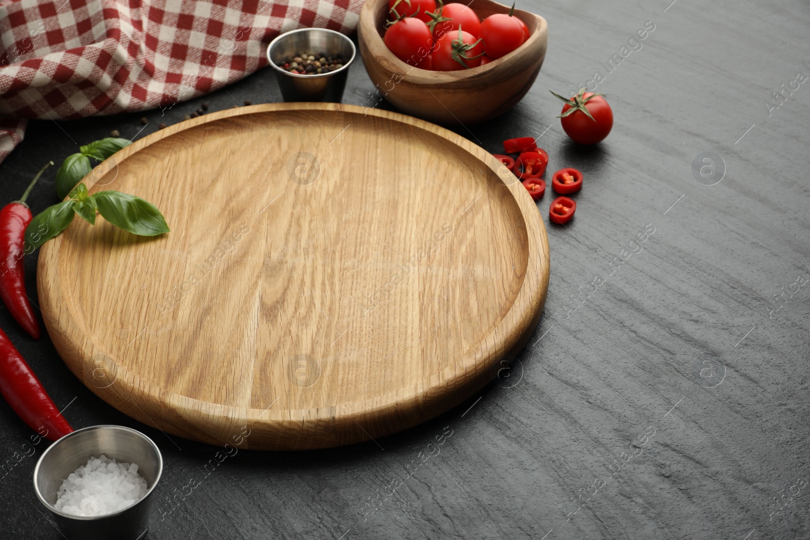 Photo of Cutting board, salt, spices, basil, tomatoes and chili peppers on black textured table. Space for text