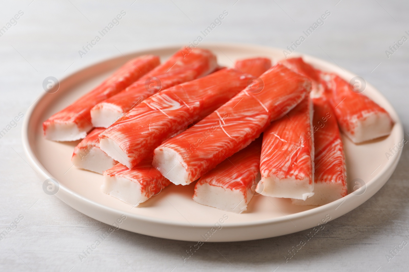 Photo of Plate of fresh crab sticks on white table, closeup