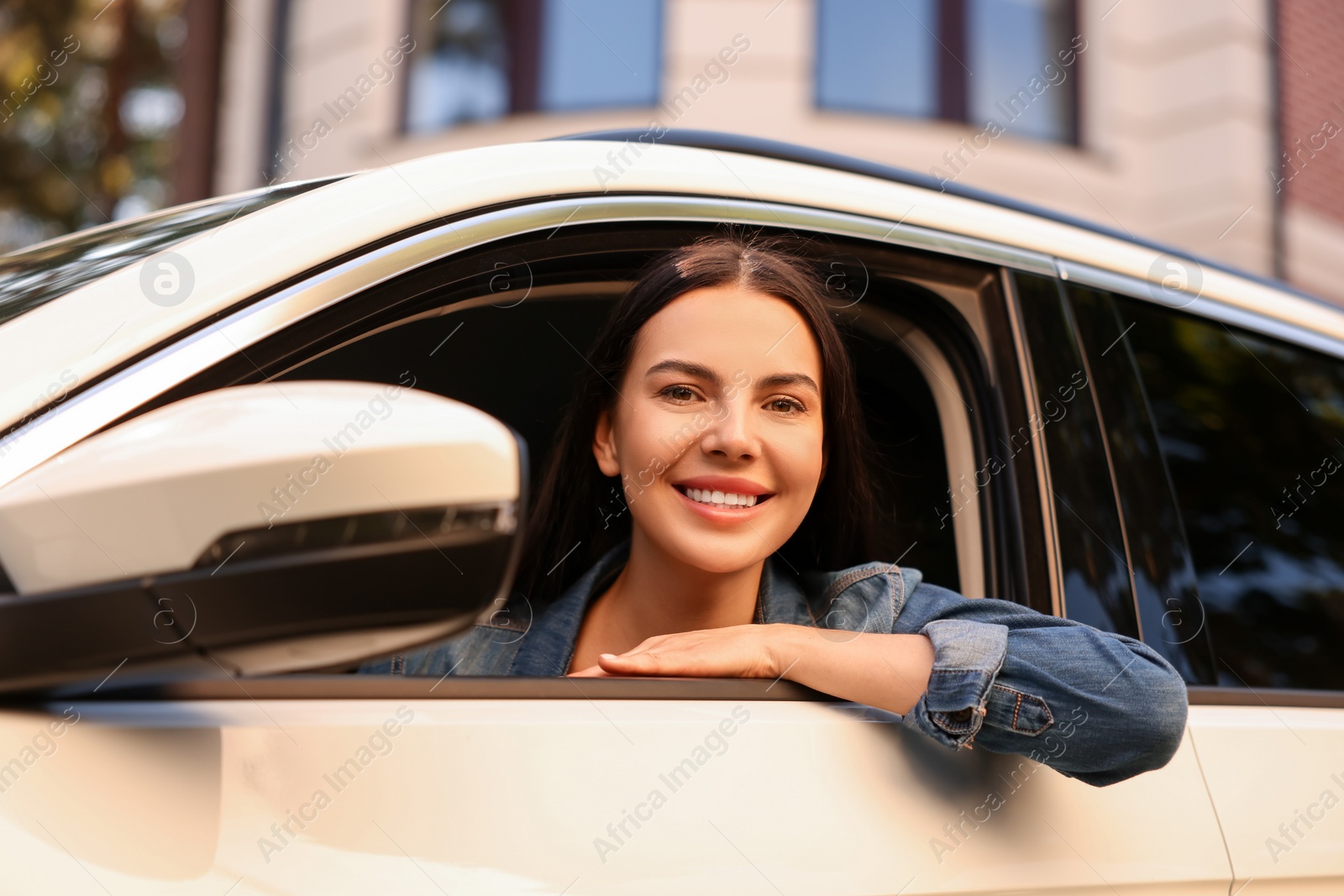 Photo of Happy young woman looking out of car window on city street, view from outside. Enjoying trip