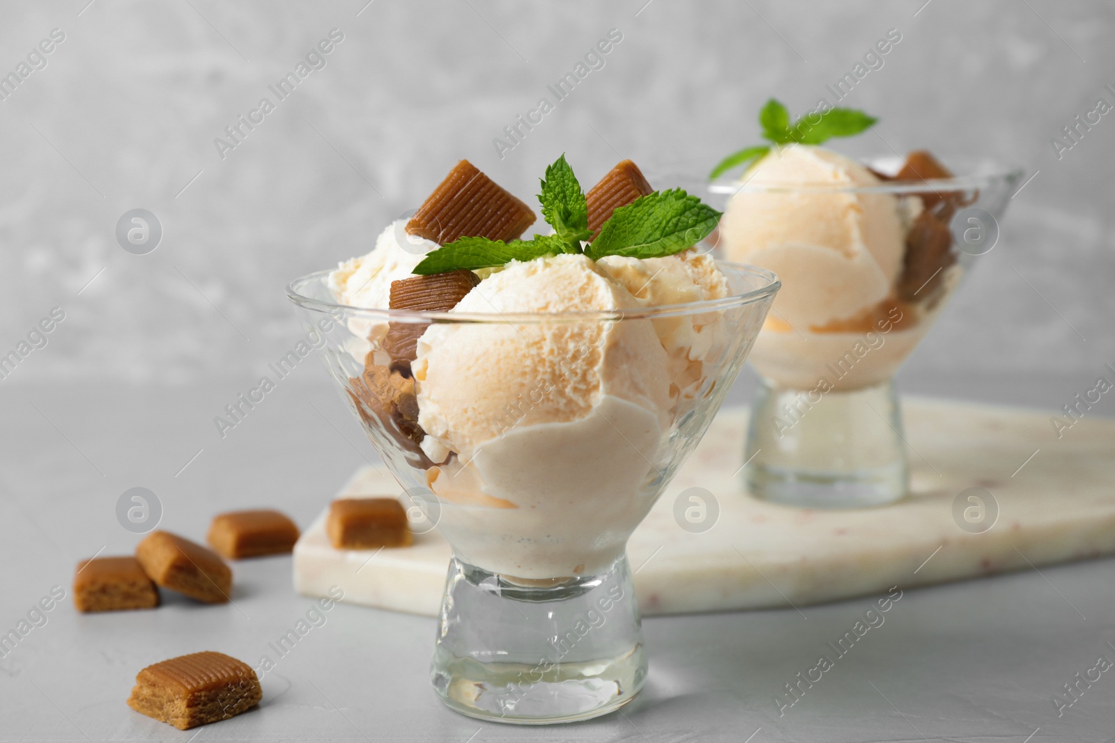 Photo of Glass dish of delicious ice cream with caramel candies and mint on light grey table