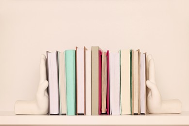 Beautiful hand shaped bookends with books on shelf near beige wall