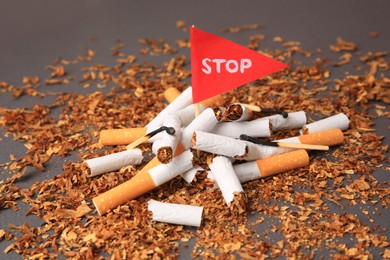 Photo of Flag with word Stop, broken cigarettes and burnt matches on dark grey background, closeup. Quitting smoking concept