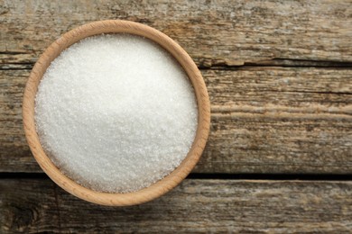 Granulated sugar in bowl on wooden table, top view. Space for text