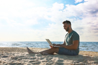 Photo of Man working with laptop on beach. Space for text