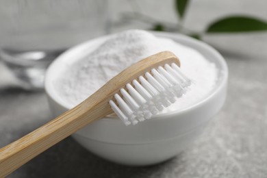 Photo of Bamboo toothbrush, green leaf and bowl of baking soda on grey table, closeup