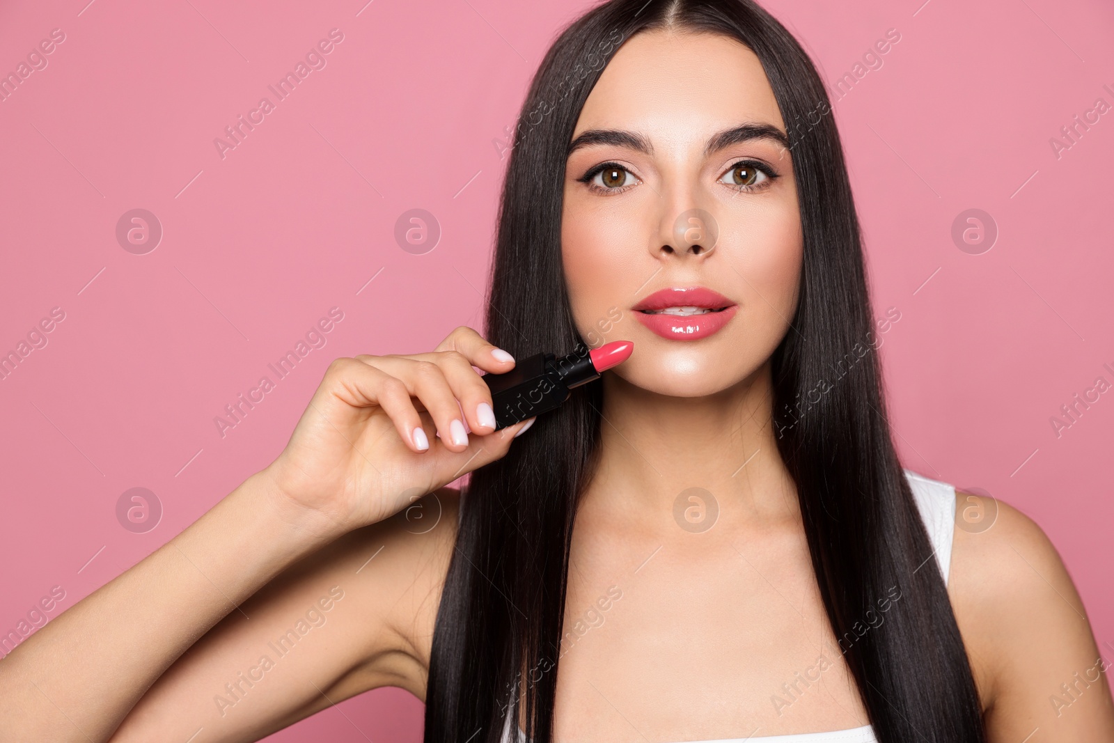 Photo of Young woman with beautiful makeup holding glossy lipstick on pink background