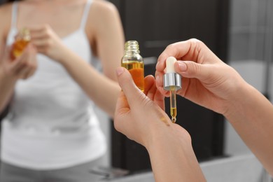 Photo of Young woman applying essential oil onto wrist in bathroom, closeup