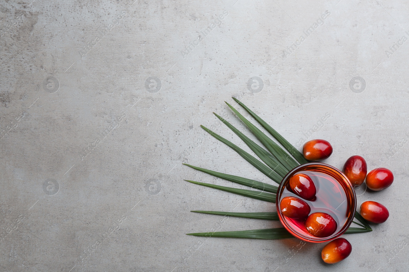 Photo of Palm oil in glass bowl with fruits and tropical leaf on grey table, flat lay. Space for text