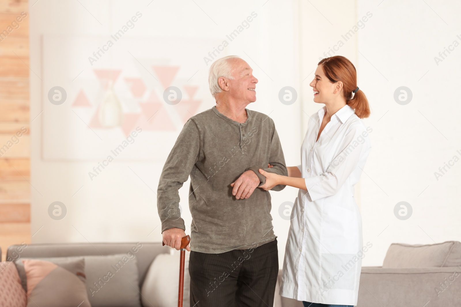 Photo of Elderly man with walking cane and female caregiver in living room