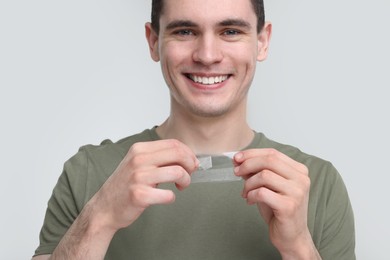 Young man with whitening strips on light grey background