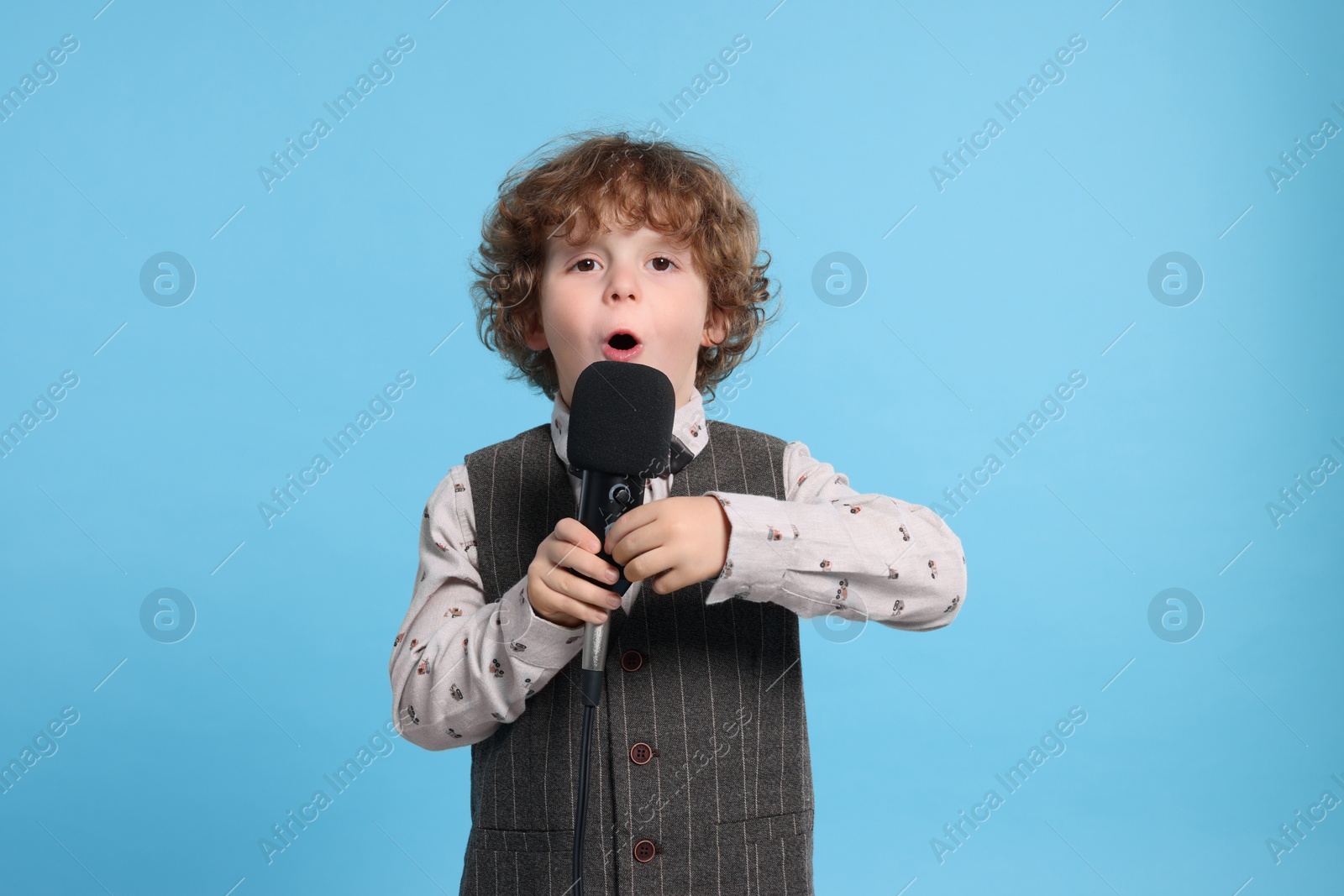 Photo of Cute little boy with microphone singing on light blue background